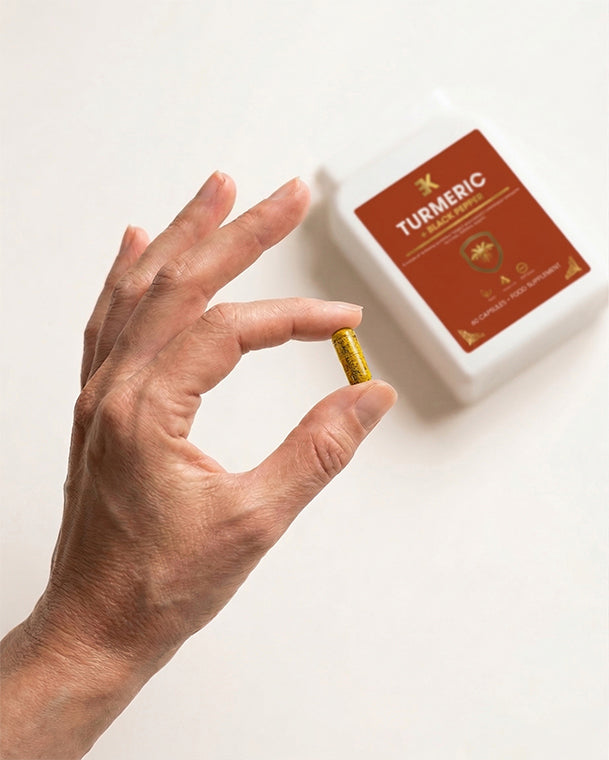 Hand holding a turmeric supplement capsule with a box labeled 'Turmeric' in the background.